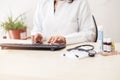 Female doctor in white lab coat,hands typing on laptop computer keyboard with medical stethoscope and medicine on the mirror desk