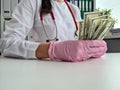 Female doctor in white medical coat holds dollars in hands