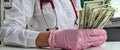 Female doctor in white medical coat holds dollars in hands