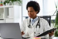 Female doctor working at her office in front of laptop computer, writing a health report Royalty Free Stock Photo