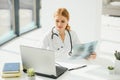 Female doctor working at office desk and smiling at camera, office interior on background. Royalty Free Stock Photo