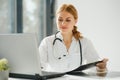 Female doctor working at office desk and smiling at camera, office interior on background. Royalty Free Stock Photo