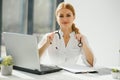Female doctor working at office desk and smiling at camera, office interior on background. Royalty Free Stock Photo