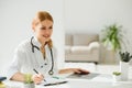 Female doctor working at office desk and smiling, office interior on background. Royalty Free Stock Photo