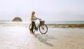 Female dressed light summer clothes have morning walk with old vintage bicycle with front basket on the lonely low tide ocean