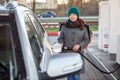 Female driver refueling car at self-service gas station, woman in coat and warm hat holding hose with nozzle and looking at camera Royalty Free Stock Photo
