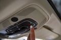 female driver`s finger presses the sos button on the ceiling panel of a modern car