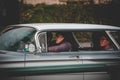 Female driving a gay shiny old car with her family in the street