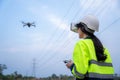 A female electrical engineer wearing vr goggles inspects site using drone survey aerial view of high voltage pylons at power