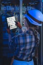 Female electrician from behind points at a tablet schematic in front of a switchboard. Digital twin. Royalty Free Stock Photo