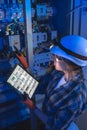 Female electrician points at breakers and reads a tablet schematic. Digital twin. Royalty Free Stock Photo