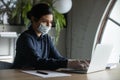 Female employee in face mask work on laptop in office