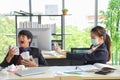 Female employee wearing medical face mask and spraying alcohol spray to her male colleague who is coughing and sneezing Royalty Free Stock Photo