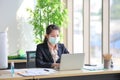 Female employee wearing medical face mask while working alone because of social distancing policy in the business office