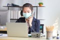 Female employee wearing medical face mask while working alone because of social distancing policy in the business office