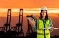 Female engineer with computer blueprint is standing infront sea port cargo crane harbor terminal Royalty Free Stock Photo