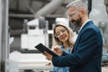 Female engineer and male production manager standing in modern industrial factory, talking about production