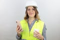 Female engineer wearing reflecting jacket and hardhat smiling happy holding smartphone and paper cup takeaway. Royalty Free Stock Photo