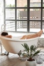 A female enjoy lies in a white bathtub and looks out the street through a large window. Back view shot