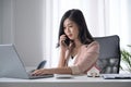 Female entrepreneur having cell phone conversation and using laptop computer at office desk. Royalty Free Stock Photo