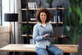 Female entrepreneur, portrait of young afro american businesswoman sitting at desk with laptop in office, looking and smiling at c Royalty Free Stock Photo