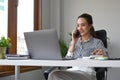 Female entrepreneur sitting at office desk with laptop and talking on mobile phone. Royalty Free Stock Photo