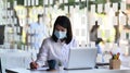 Female entrepreneur wearing face mask while working on a computer and writing notes in office.