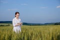 Female environmentalist scientist in a white coat in a green field of unripe ears of corn and recording data on a tablet