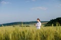 Female environmentalist scientist in a white coat in a green field of unripe ears of corn and recording data on a tablet