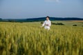 Female environmentalist scientist in a white coat in a green field of unripe ears of corn and recording data on a tablet