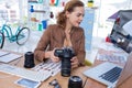 Female executive holding digital camera while looking at laptop Royalty Free Stock Photo