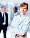 Female executive standing casually with colleagues in background. Business woman smiling while standing with arms folded Royalty Free Stock Photo