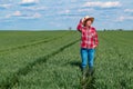 Female farmer agronomist standing in young green wheat field