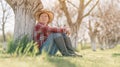 Female farmer relaxing and resting in organic walnut orchard, sitting under the fruit tree in spring