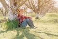 Female farmer relaxing and resting in organic walnut orchard, sitting under the fruit tree in spring