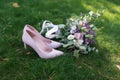 Female fashion pink wedding shoes with elegant bride`s bouquet in pastel tones on green grass background. Royalty Free Stock Photo