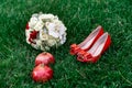 Female fashion red wedding shoes with bride`s bouquet of white roses and two red garnets on green grass background Royalty Free Stock Photo