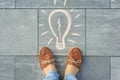 Female feet with abstract image drawing of light bulb written on grey sidewalk