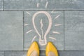 Female feet with abstract image drawing of light bulb written on grey sidewalk