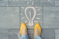 Female feet with abstract image drawing of light bulb written on grey sidewalk