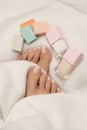 Female feet with aesthetic french pedi with pedicure accessories and nail polishes on white blanket.