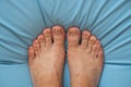 Female feet barefoot on a light blue mattress, top to bottom view