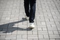 Female feet in black jeans and white sneakers walking on the sidewalk in the city. Royalty Free Stock Photo