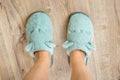 Female feet in blue cozy slippers on a wooden floor at bedroom close-up. Concepts of comfy soft fleece home shoes and warm