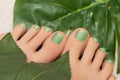 Female feet with green glitter nail design. Green nail polish pedicure and greel leaves on background Royalty Free Stock Photo