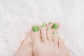 Female feet with green nail design. Glitter green nail polish pedicure on white fluffy background Royalty Free Stock Photo