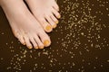 Female feet with orange pedicure. Woman legs with glitter orange nail design on brown fabric with orange paillettes