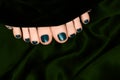 Female feet with pine nail design. Black nail polish pedicure on dark green fabric background Royalty Free Stock Photo