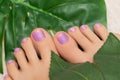 Female feet with pink glitter nail design. Pink nail polish pedicure and greel leaves on background Royalty Free Stock Photo