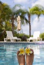 Female feet with plumeria flowers near swimming pool surrounded by the palm trees. Selective focus, blurred background. Royalty Free Stock Photo